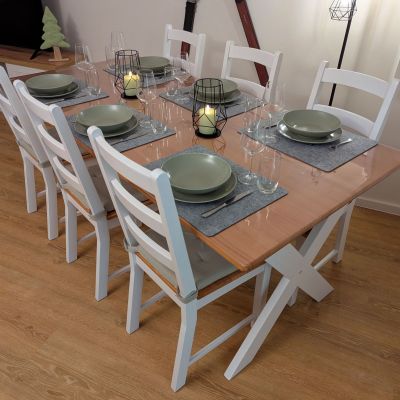 Esstisch im Wohnzimmer ist für 6 Personen gedeckt, mit Tellern, Besteck und Gläsern, auf dem Tisch leuchten Kerzen.